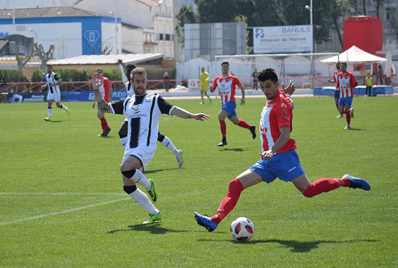 Álex Herrera centrando un balón e intentado ser tapado por José Higón