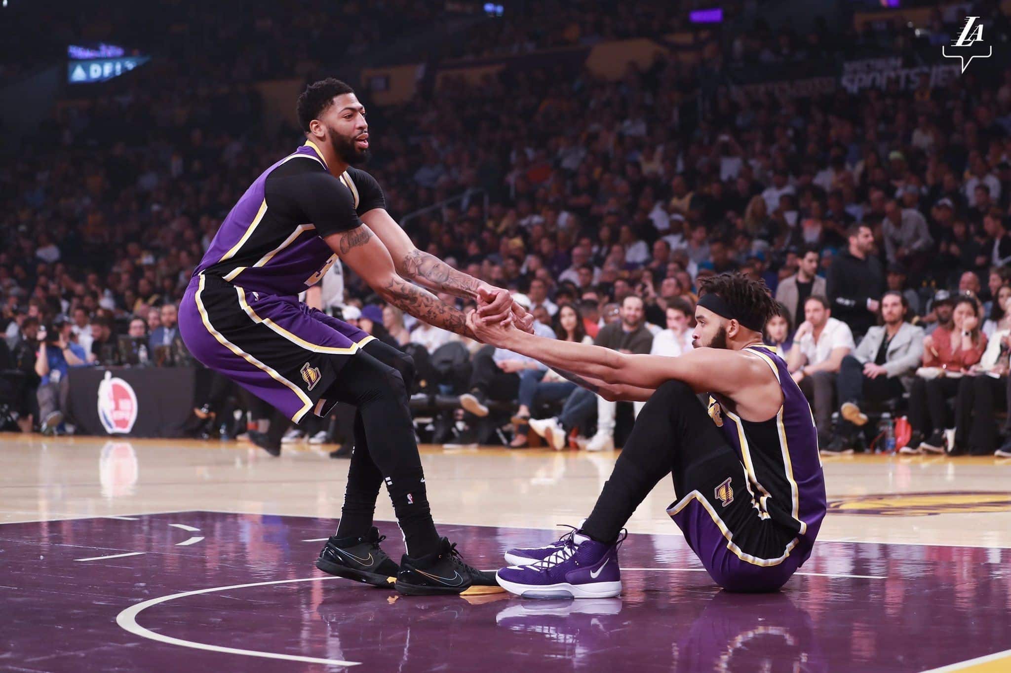 Anthony Davis ayuda a levantarse a JaVale McGee durante un partido. Imagen vía: @Lakers
