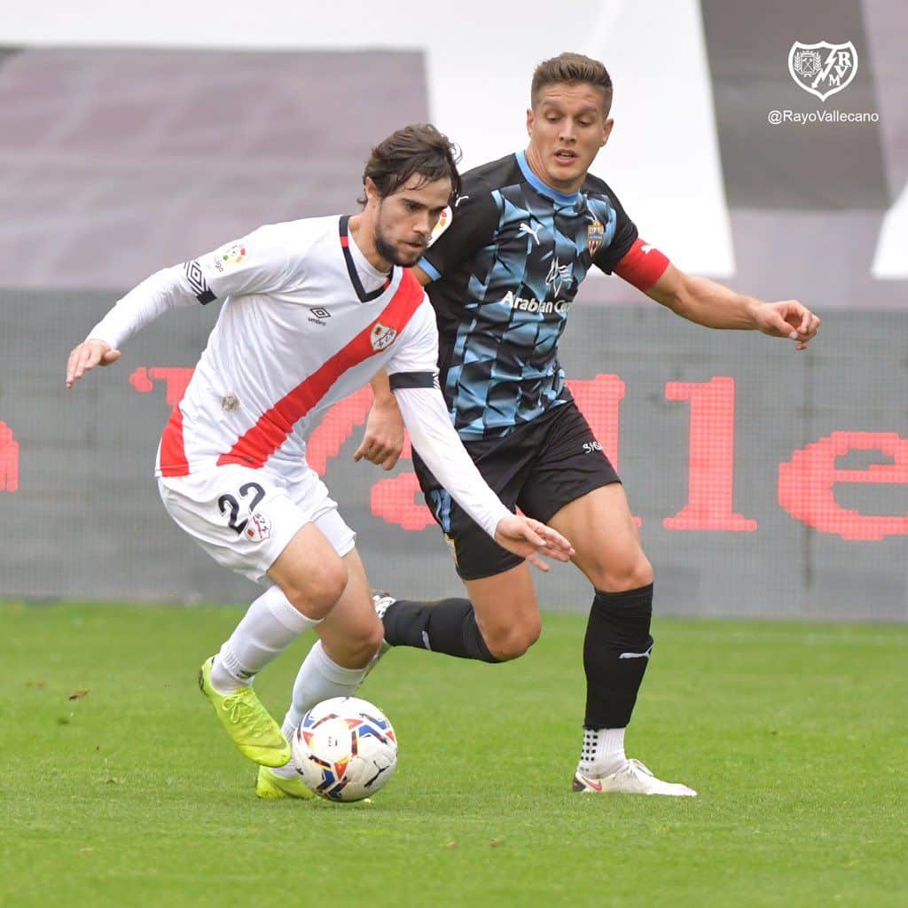 Pozo conduce un balón ante la presencia de Corpas (@Rayo Vallecano)